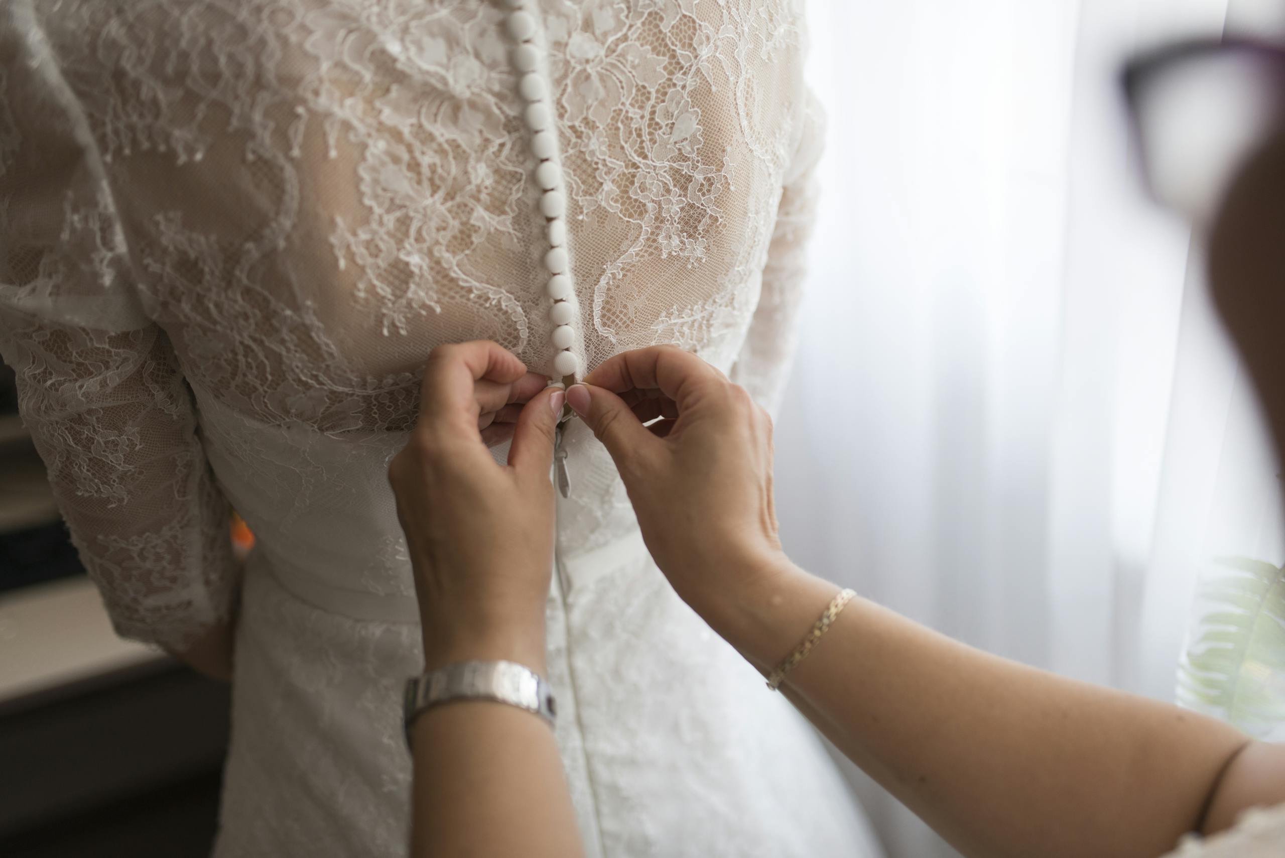 A bride getting her dress adjusted by a family member indoors, highlighting a touching wedding preparation moment.
